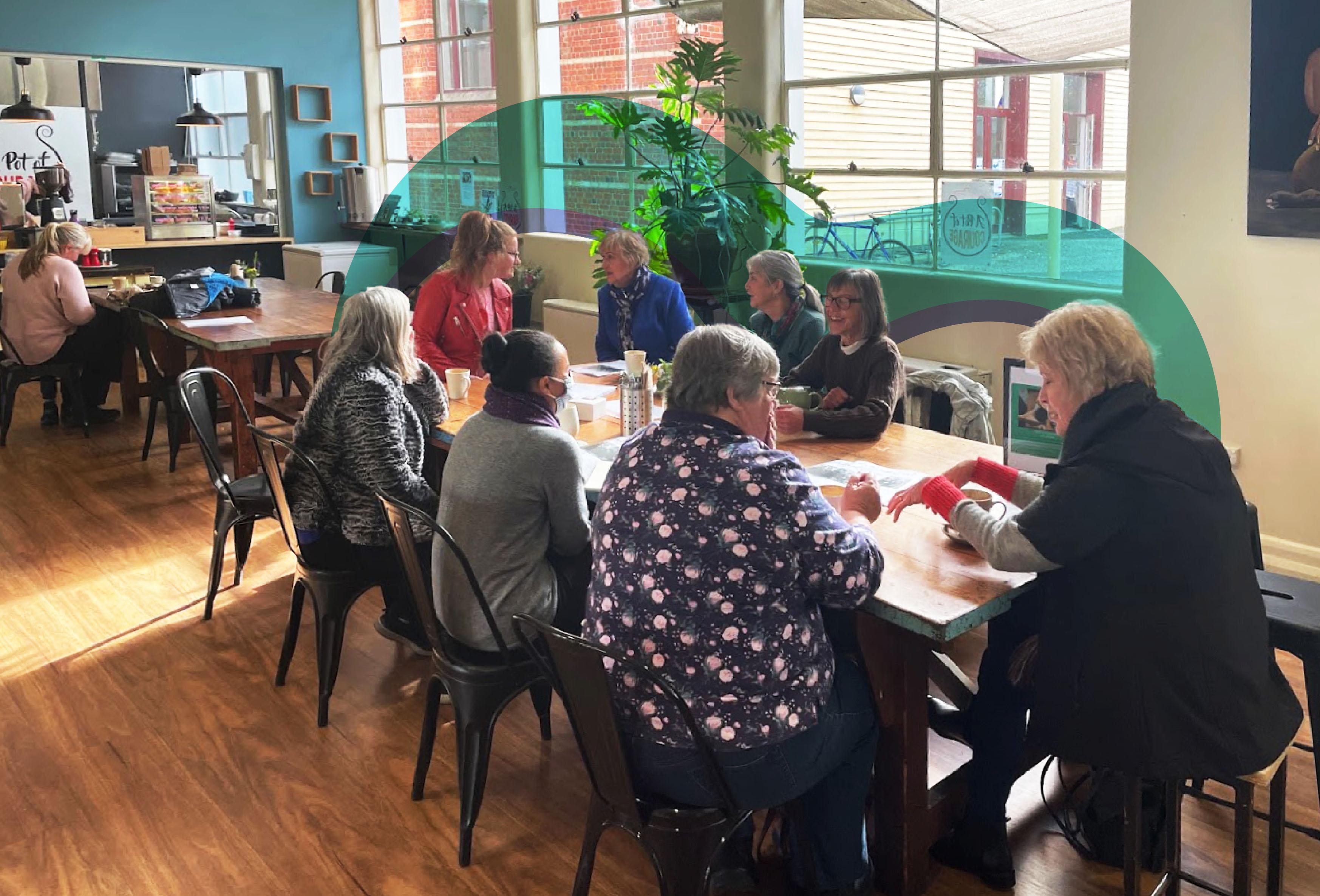 A long table with a group of people enjoying discussion and connection at a Chatty Cafe location.